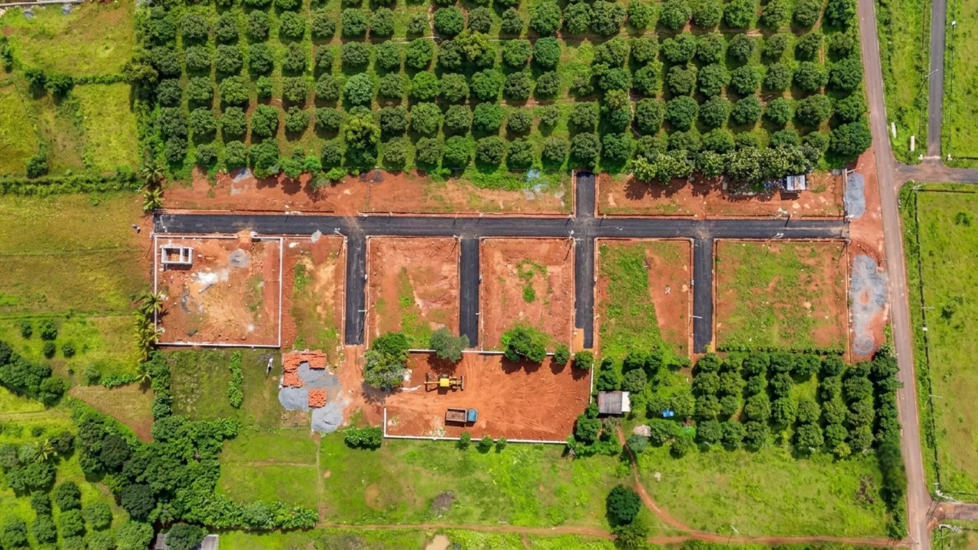 Top-down view of a newly laid plot layout with tarred roads amid orchards